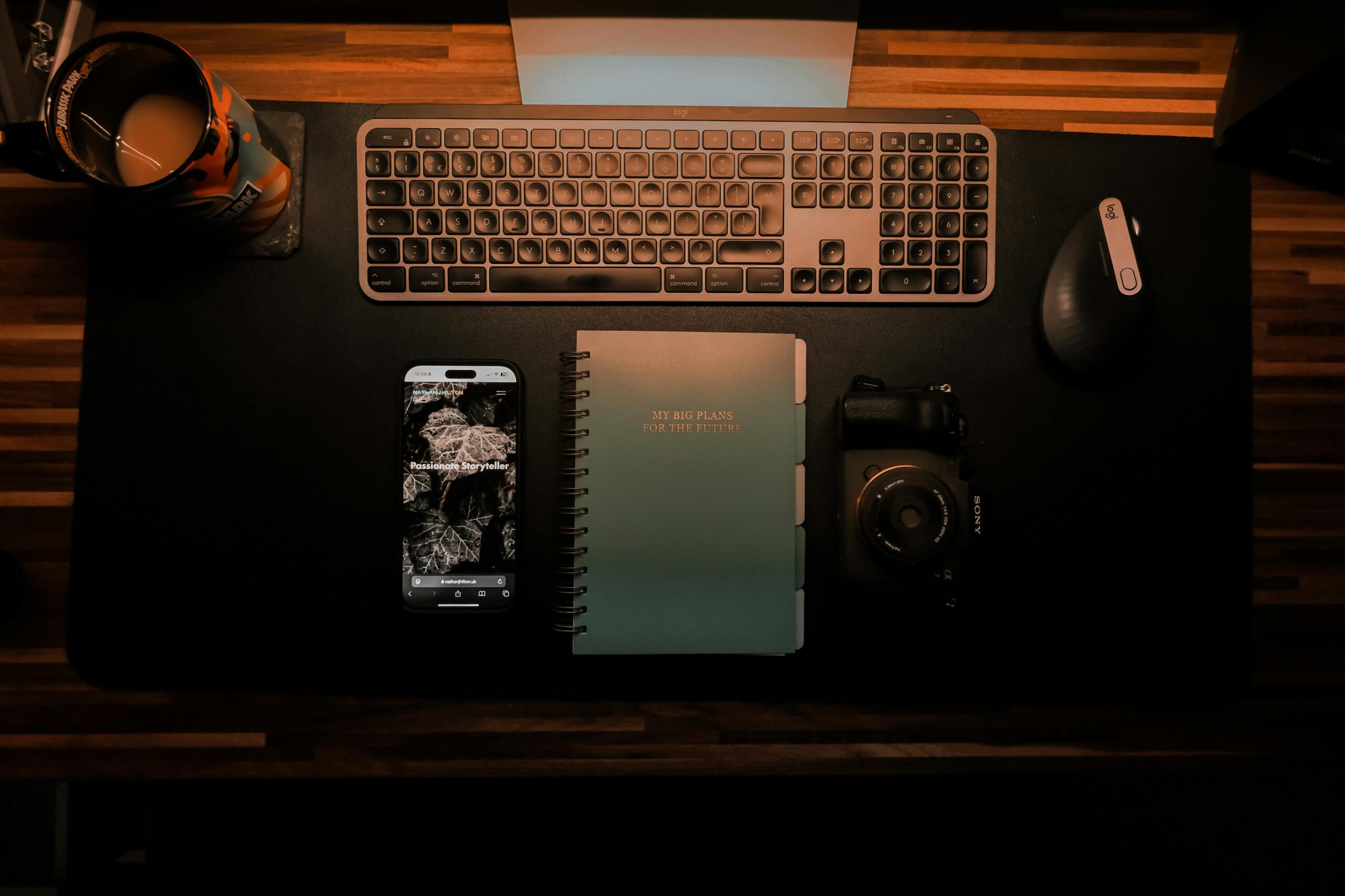 Top-down view of an organized desk setup featuring keyboard, camera, notebook, and smartphone for creative planning.