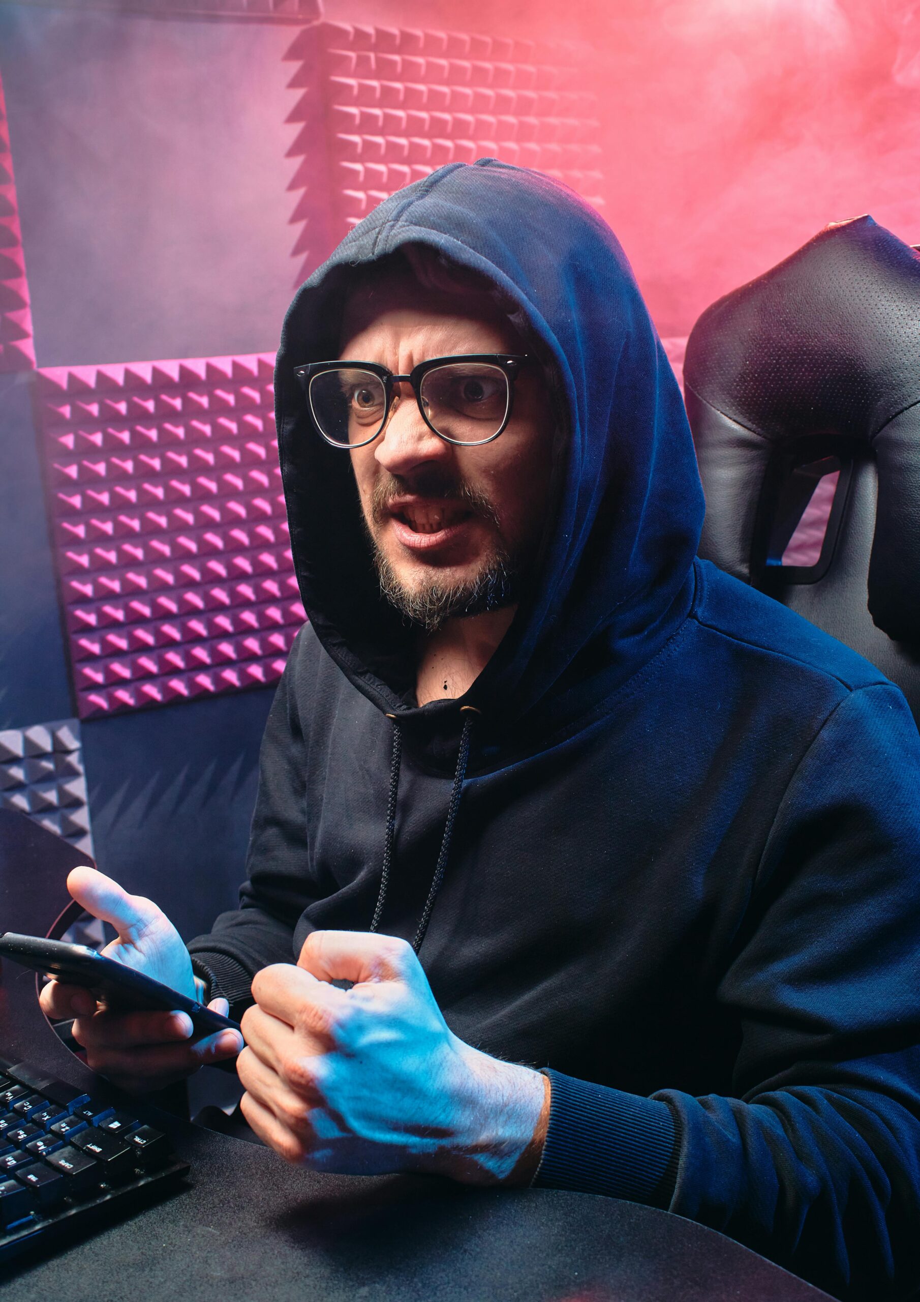 Focused man in hoodies with glasses, holding smartphone, conveying cybersecurity theme.