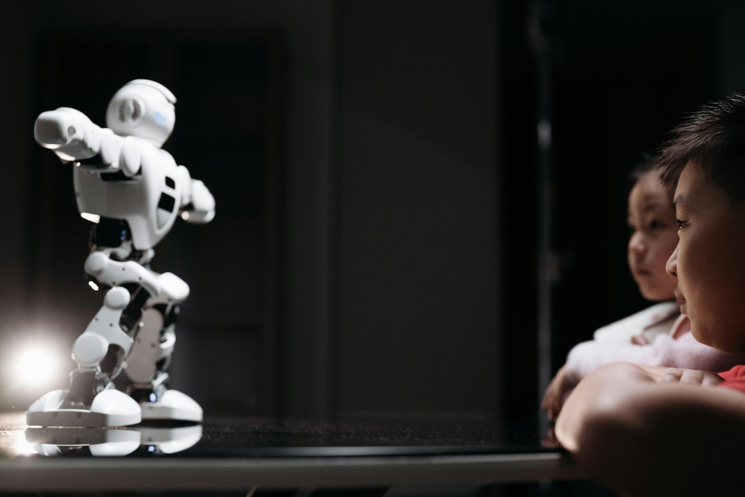 Children watching a humanoid robot toy on a reflective surface, showcasing innovation and curiosity.